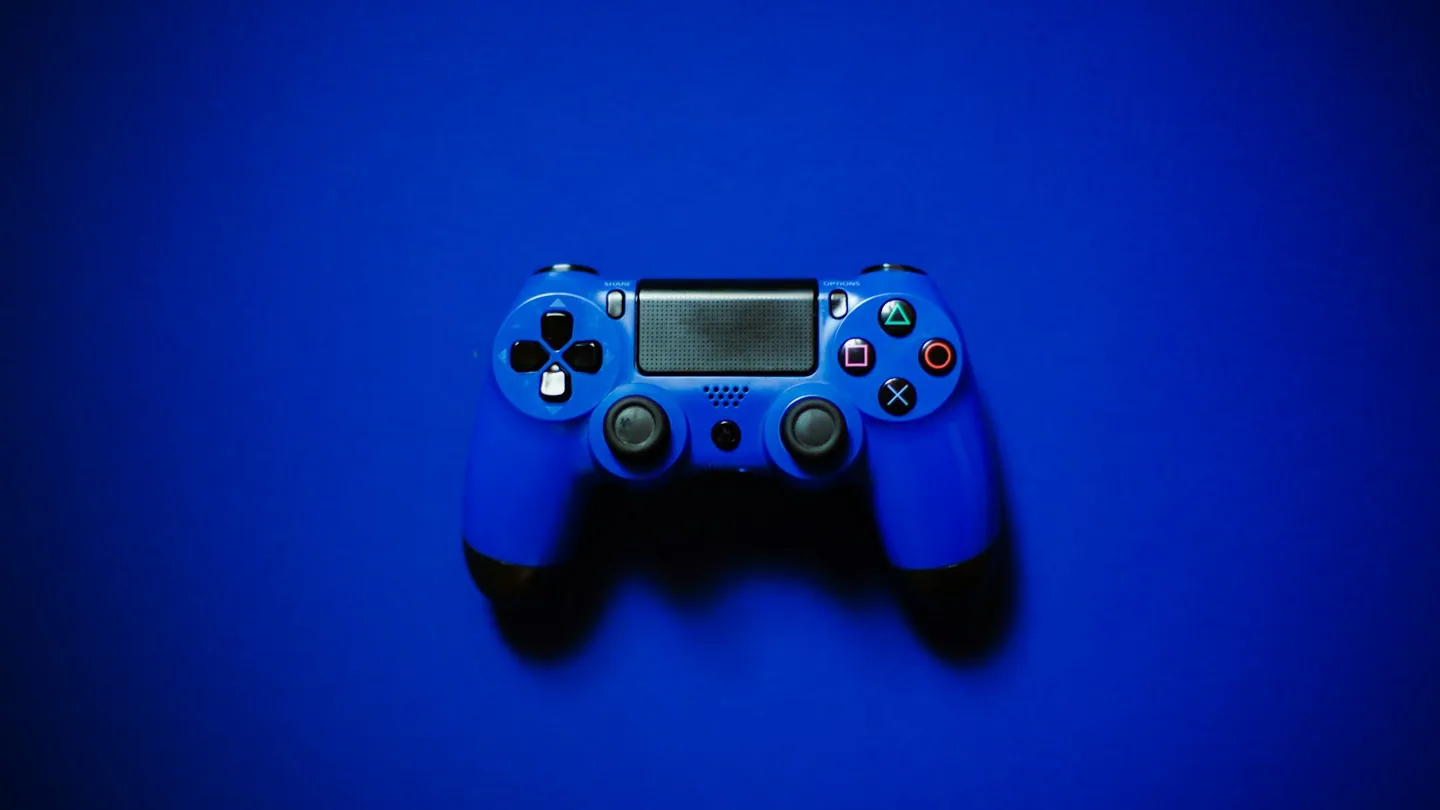 Foto ilustrativa: controle de videogame azul sobre fundo colorido. Imagem do acervo Unsplash.