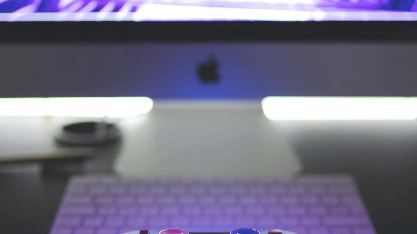 Foto ilustrativa: controle diante de monitor com iluminação roxa. Imagem do acervo Unsplash.