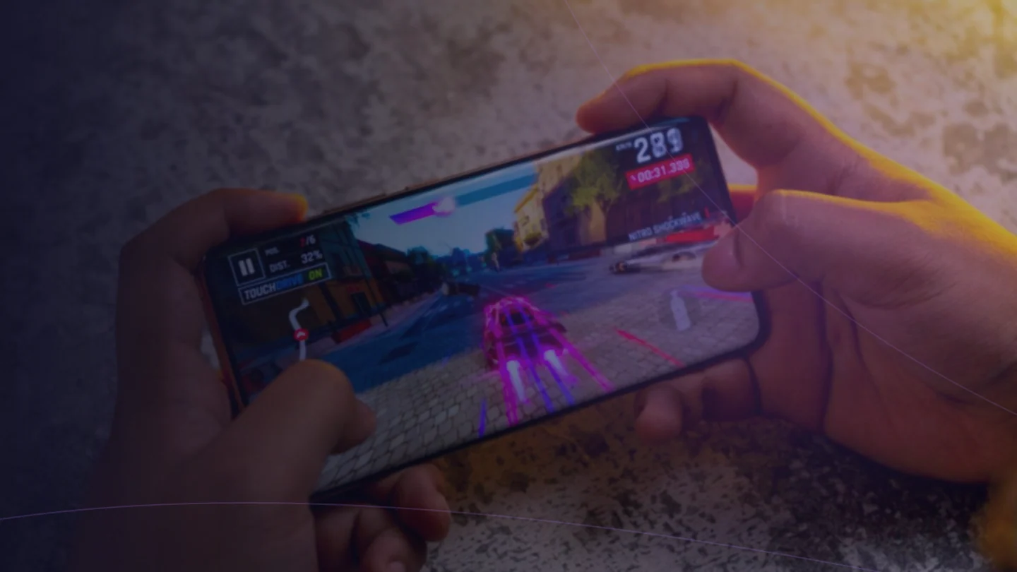 Pessoa jogando no smartphone em uma cena de videogame, com iluminação colorida.