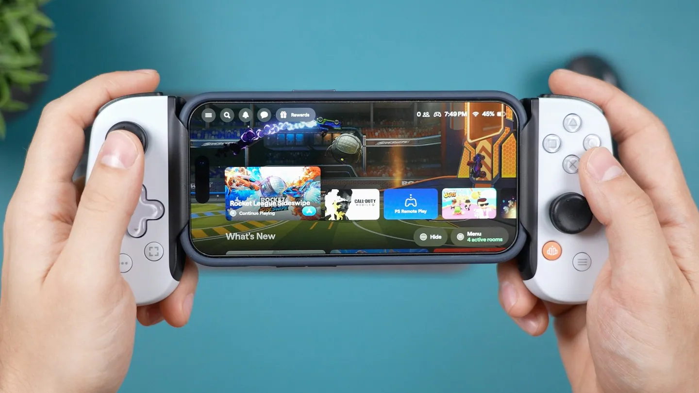 Foto ilustrativa de Daniel Romero (Unsplash): mãos segurando um iPhone com controle para jogos móveis; não representa os títulos anunciados.